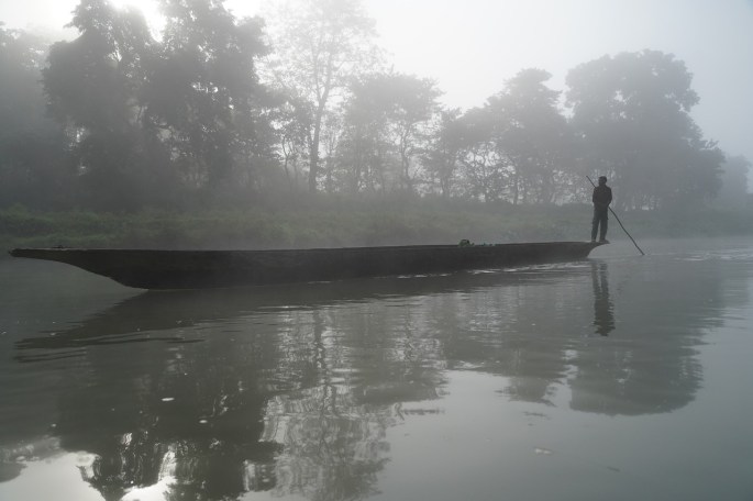 Das Bild zeigt einen Fährmann, der auf seinem langen Boot steht. Die Fährstange ist ins Wasser getaucht.