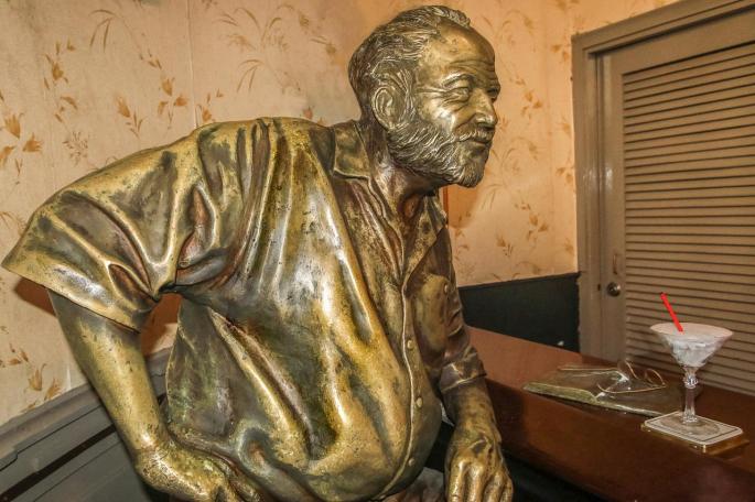 Das Bild zeigt eine Statue von Ernest Hemingway, der Dichter lehnt sich an einen Tresen.