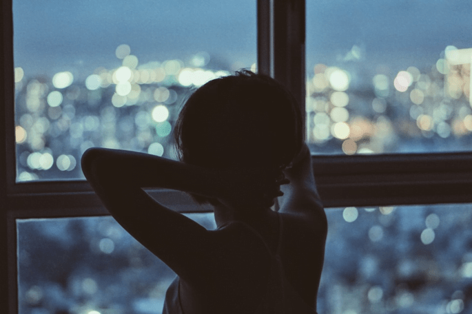 Das Bild zeigt eine aus einem Fenster blickende junge Frau.d